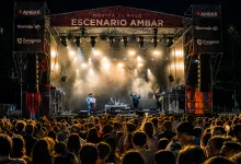 Outdoor Concert Stage at Night with Bright Lights and a Band Performing in Front of a Large Crowd Under a Red Banner That Reads escenario Ambar María Arnal Y Nortec Ponen El Broche Final a Música Al Raso Zaragozala   Qué Hacer En Zaragoza