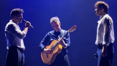 Three Male Musicians Perform on Stage One Sings with a Microphone the Center Guitarist Plays an Acoustic Guitar Under Blue Stage Lighting Zaragozala | Agenda Cultural Ocio Y Planes En Zaragoza Zaragozala   Qué Hacer En Zaragoza