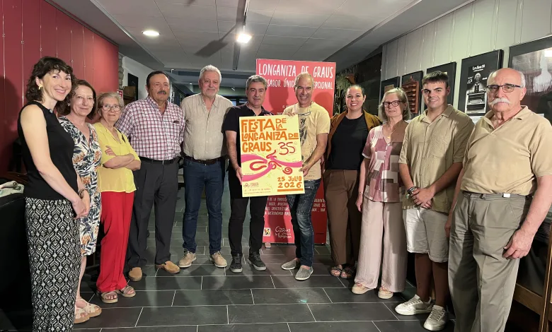 Group of Adults Posing for a Photo Indoors Around a Festival Poster and Red Banner That Reads Longaniza De Graus All Smiling at the Camera La Fiesta De La Longaniza De Graus 2026 Ya Tiene Cartel Zaragozala Qué Hacer En Zaragoza
