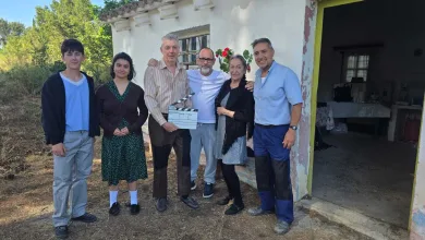 Six People Stand Outdoors by a White Weathered Building a Man in the Center Holds a Film Clapperboard Smiling with the Group El Festival De Cine De Fuentes Rueda En Rodén El Spot De Su 30 Aniversario Inspirado En Los Santos Inocentes Zaragozala   Qué Hacer En Zaragoza
