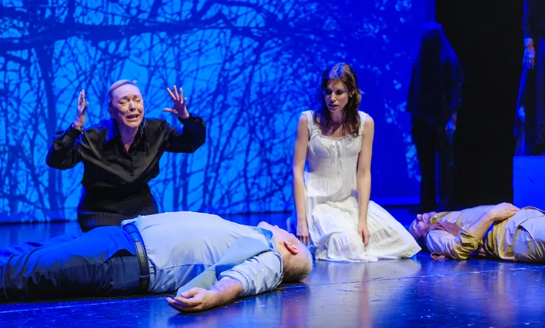 Two Actors on a Blue lit Stage Kneel Beside Motionless Bodies As a Woman in Black Gestures Dramatically While a Woman in a White Dress Looks On Arbolé Celebra La Vi Muestra De Teatro Amateur Zaragozala Qué Hacer En Zaragoza