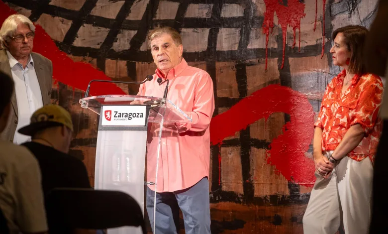 Man in Coral Shirt Speaks at a Transparent Podium with Two Microphones Flanked by an Older Man in a Gray Suit and a Woman in a Red Patterned Blouse Zaragoza Ayuntamiento Sign on the Lectern Zaragozala | Agenda Cultural Ocio Y Planes En Zaragoza Página 1018 Zaragozala Qué Hacer En Zaragoza