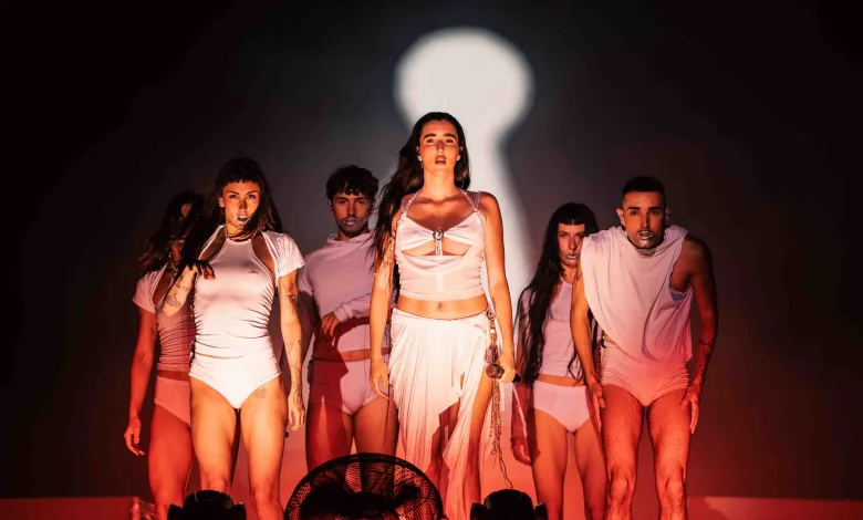 a Group of Dancers in White Outfits Standing on Stage Under Red Lighting with a Large Bright Spotlight Behind Them Judeline Samuraï Y Elem Toman Pirineos Sur 2026 Zaragozala   Qué Hacer En Zaragoza