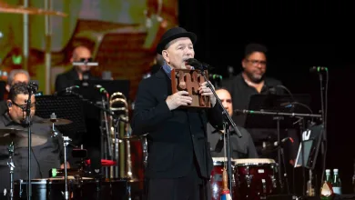 Male Singer in a Black Suit and Hat Performs on Stage Holding a Wooden Perforated Instrument Near His Mouth As a Band Plays Behind Him on Drums and Brass Rubén Blades Recibe El Premio Pirineos Sur 2026 Zaragozala Qué Hacer En Zaragoza