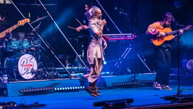 Female Singer Mid jump Microphone in Hand Performing on a Blue lit Stage with a Guitarist on the Right and a Drummer on the Left in the Background Chambao Y Lia Kali Llenan Pirineos Sur 2026 Zaragozala Qué Hacer En Zaragoza