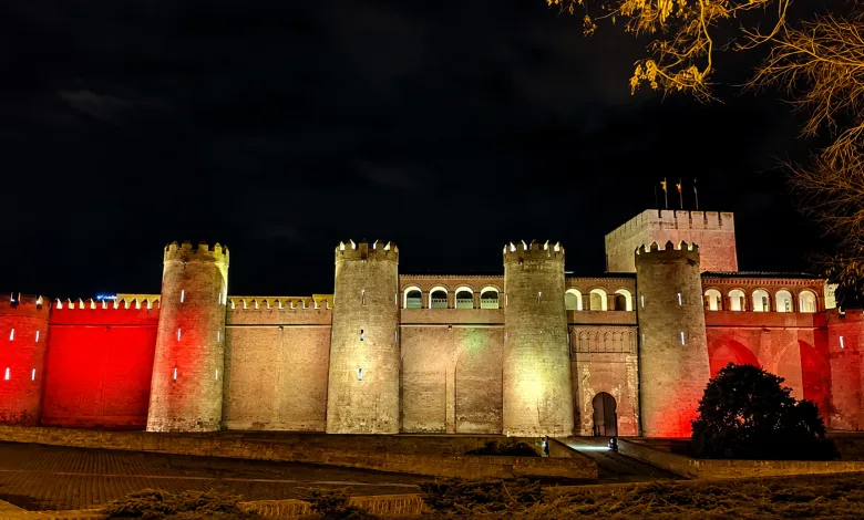 Night View of a Medieval Fortress with Tall Cylindrical Towers Illuminated Red and Amber Along the Wall at Night La Aljafería Se Ilumina Por La Final España argentina Zaragozala Qué Hacer En Zaragoza