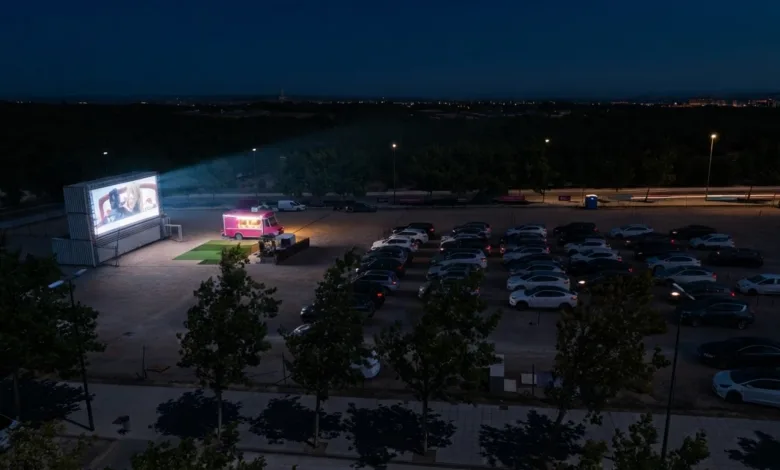 Drive in Movie Theater at Night with a Bright Screen on the Left a Pink Food Truck Nearby and Rows of Parked Cars Under Dim Streetlights Puerto Venecia Abre Este Sábado Un Autocine De Verano Zaragozala Qué Hacer En Zaragoza