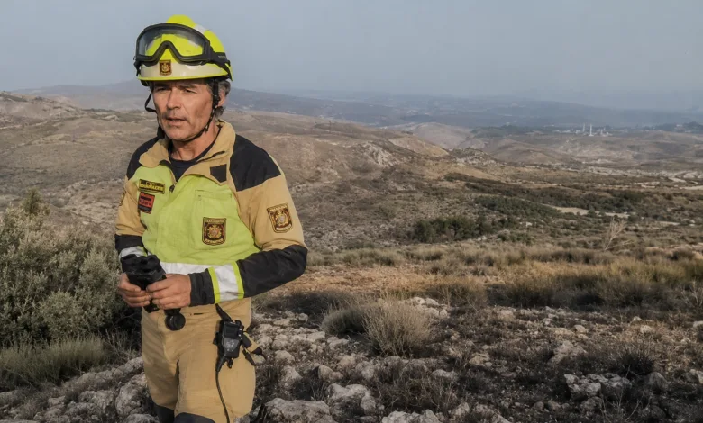 Firefighter in Tan Turnout Gear and Yellow Helmet Stands on Rocky Hillside Overlooking a Dry Valley Incendio Forestal Ejulve Bomberos Zaragoza Apoyan Evacuación Zaragozala Qué Hacer En Zaragoza