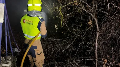 Firefighter Wearing a Yellow Helmet and Highvisibility Jacket Labeled bomberos Zaragoza Handling a Yellow Hose at Night by Leafless Brush Area Los Bomberos De Zaragoza Protegen Luesia Del Incendio Zaragozala Qué Hacer En Zaragoza