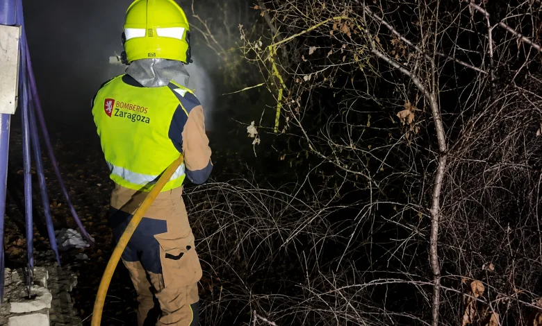 Firefighter Wearing a Yellow Helmet and Highvisibility Jacket Labeled bomberos Zaragoza Handling a Yellow Hose at Night by Leafless Brush Area Los Bomberos De Zaragoza Protegen Luesia Del Incendio Zaragozala Qué Hacer En Zaragoza