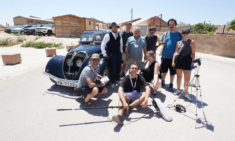 Film Crew Posing Beside a Classic Black Car on a Sunny Street with Gear and a Tripod Nearby el Aquello Gana Belchite De Película 2026 Zaragozala Qué Hacer En Zaragoza