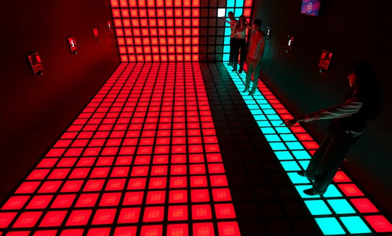 People Standing on a Glowing Grid of Red Led Floor Tiles with a Turquoise Strip Along the Right Edge in a Dark Room Dónde Jugar a El Suelo Es Lava En Zaragoza Zaragozala Qué Hacer En Zaragoza