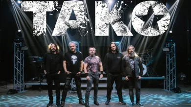 Six member Rock Band Posing on Stage Beneath a Large Distressed White Tako Sign with Bright Stage Lights Tako Llena Veruela En Su Concierto Del 40 Aniversario Zaragozala   Qué Hacer En Zaragoza