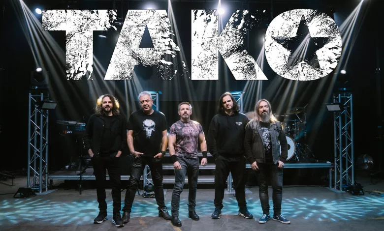 Six member Rock Band Posing on Stage Beneath a Large Distressed White Tako Sign with Bright Stage Lights Tako Llena Veruela En Su Concierto Del 40 Aniversario Zaragozala Qué Hacer En Zaragoza