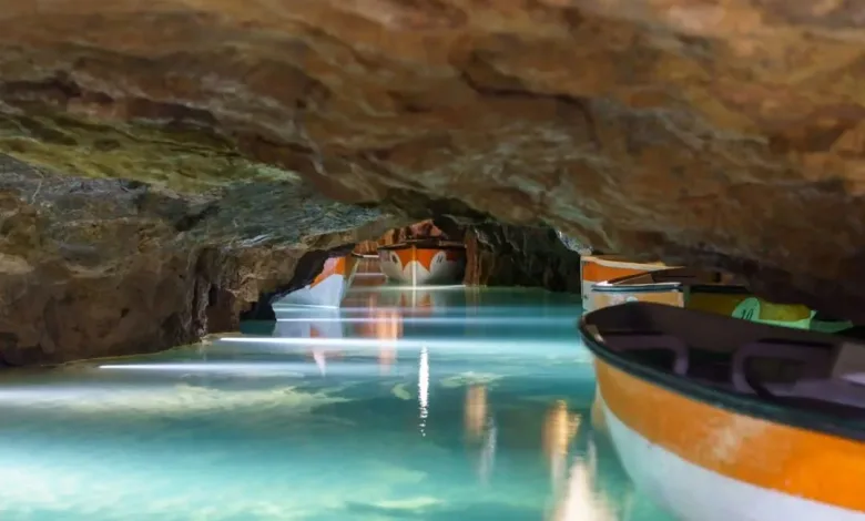 Cave with turquoise water and several colorful boats docked along a narrow cavern wall.