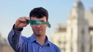 Man in Blue Shirt Holding Green Cardboard 3d Glasses Toward the Camera Logo Visible Caja Rural De Aragón outdoor City Background Gafas Eclipse Solar Aragón Dónde Conseguirlas Gratis Zaragozala Qué Hacer En Zaragoza