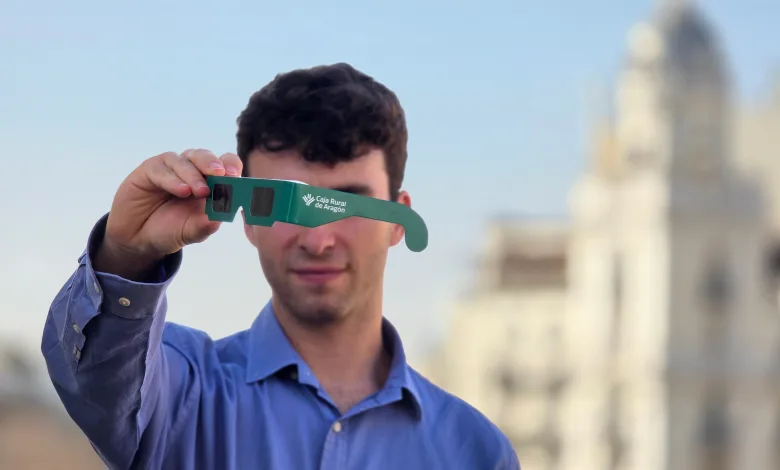 Man in Blue Shirt Holding Green Cardboard 3d Glasses Toward the Camera Logo Visible Caja Rural De Aragón outdoor City Background Gafas Eclipse Solar Aragón Dónde Conseguirlas Gratis Zaragozala Qué Hacer En Zaragoza