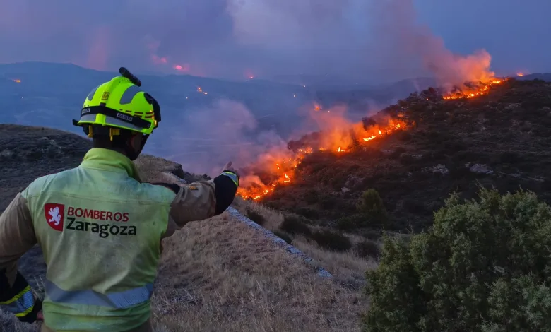 Firefighter in a Yellow Helmet and Jacket Overlooking a Wildfire on a Hillside with Smoke and Flames in the Distance zaragoza Firefighters Los Bomberos De Zaragoza Se Suman Al Operativo Del Incendio De Orés Zaragozala Qué Hacer En Zaragoza