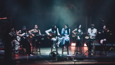 Group of Diverse Musicians on a Dimly Lit Stage Playing Guitars and Singing into Microphones During a Live Concert Valeria Castro Y Carlos Ares Llenan En Pirineos Sur 2026 Zaragozala Qué Hacer En Zaragoza