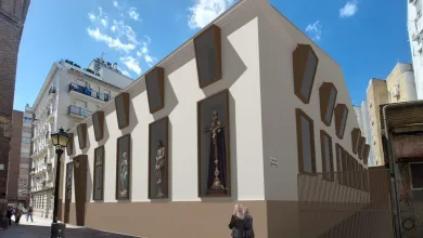 Modern beige wall with brown-framed display niches holding religious statues along a sunny urban street.