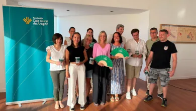 Group of ten adults posing indoors at an event, some holding awards and green fans, with a teal Fundación Caja Rural de Aragón banner on the left.