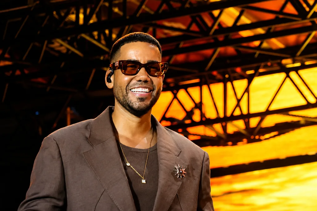 Male Performer on Stage in a Brown Blazer and Sunglasses Smiling Against Warm Orange Lighting Romeo Santos Y Prince Royce Conquistan Zaragoza a Ritmo De Bachata Zaragozala   Qué Hacer En Zaragoza