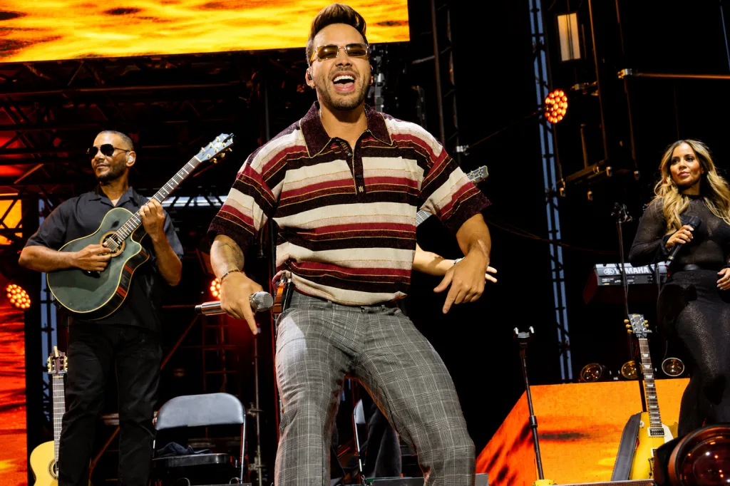 Lead Singer Center Stage Wearing a Striped Shirt and Sunglasses Singing into a Mic with a Guitarist Left and a Female Vocalist Right on an Orange lit Stage Romeo Santos Y Prince Royce Conquistan Zaragoza a Ritmo De Bachata Zaragozala   Qué Hacer En Zaragoza