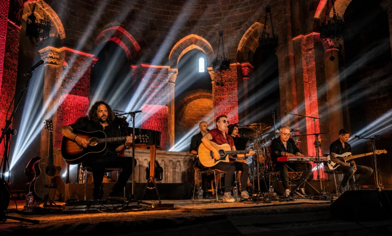 Live band performing on a historic stone-arched stage bathed in red and white spotlight beams.
