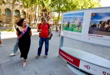 Two Pedestrians Look at a Large Outdoor Display Board with Sports Photos in a Sunny City Plaza Zaragozala | Agenda Cultural Ocio Y Planes En Zaragoza Zaragozala   Qué Hacer En Zaragoza