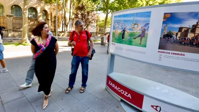 Two Pedestrians Look at a Large Outdoor Display Board with Sports Photos in a Sunny City Plaza Zaragozala | Agenda Cultural Ocio Y Planes En Zaragoza Zaragozala   Qué Hacer En Zaragoza