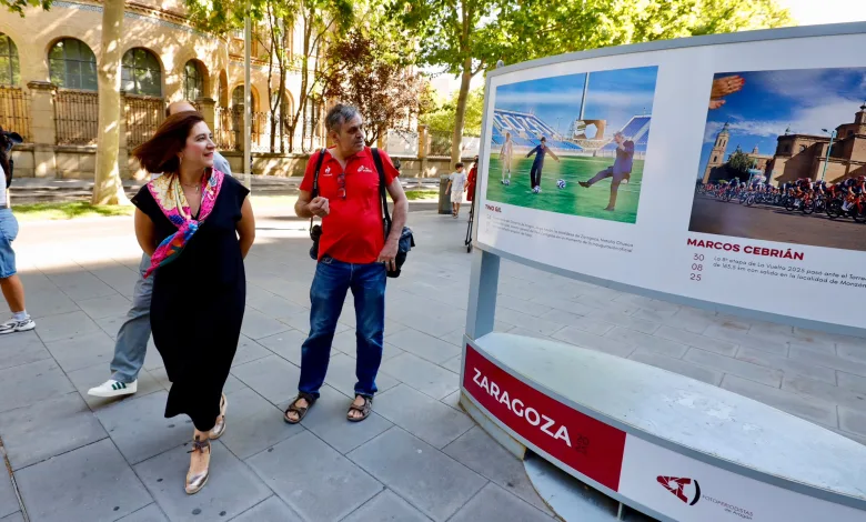Two Pedestrians Look at a Large Outdoor Display Board with Sports Photos in a Sunny City Plaza Zaragozala | Agenda Cultural Ocio Y Planes En Zaragoza Zaragozala   Qué Hacer En Zaragoza