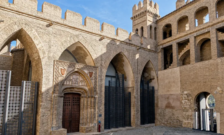Stone Fortress with Arched Entrance and Crenellated Walls Under a Blue Sky Medieval Brickwork and Decorative Doorway Front Center El Mudéjar De La Aljafería Qué Ver Y Por Qué Es único Zaragozala Qué Hacer En Zaragoza