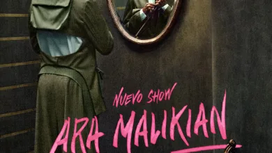 Man in a Green Coat Adjusts His Tie While Facing an Ornate Wall Mirror a Violin Rests on the Floor Beside a Bold Pink Poster That Reads art Malikian Intruso Zaragozala | Agenda Cultural Ocio Y Planes En Zaragoza Zaragozala   Qué Hacer En Zaragoza