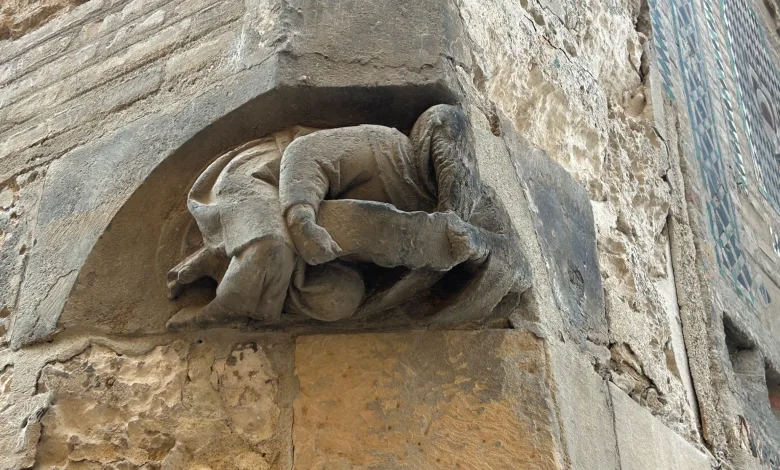 Stone Relief Depicting a Reclining Figure Carved into a Weathered Rock Wall with a Blue Geometric Tile Mural to the Right La Extraña Figura En La Seo De Zaragoza Que Pasa Desapercibida Zaragozala Qué Hacer En Zaragoza