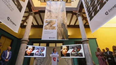 Banners Hang from a Vaulted Ceiling in a Museum like Hall with Two Marble Columns and People Viewing Portrait Displays at a Zaragoza Event Likely a City Exhibition Marca Turística De Zaragoza Dos Premios Red Dot 2026 Zaragozala   Qué Hacer En Zaragoza