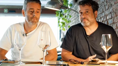 Two Men Sit at a Brick walled Restaurant Table with Empty Wine Glasses in Front of Them Appearing to Chat Seriously One Wears a White Shirt the Other a Black Shirt Reservas Fantasma En Zaragoza El Caso Viral De La Miguería Zaragozala Qué Hacer En Zaragoza