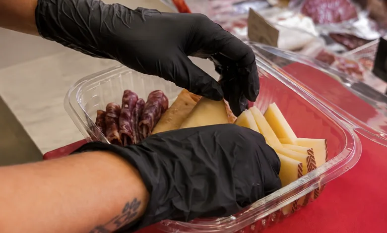 Gloved Hands Arrange Cheese and Salami Slices in a Clear Plastic Container on a Red Surface La Charcutería Que Regala Gafas Con Su Pack Picnic Del Eclipse Zaragozala Qué Hacer En Zaragoza
