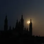 Silhouetted Domed Cathedral Spires Against a Darkening Sky with a Solar Eclipse Peeking Behind the Tallest Tower and a Golden Sunset Reflected on the Water Miles De Personas Observan El Eclipse Total En Zaragoza Zaragozala Qué Hacer En Zaragoza
